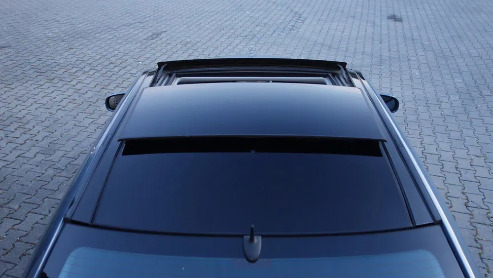 Top-down view of a dark-colored car with its sunroof partially retracted, parked on an empty paved surface made of interlocking bricks.