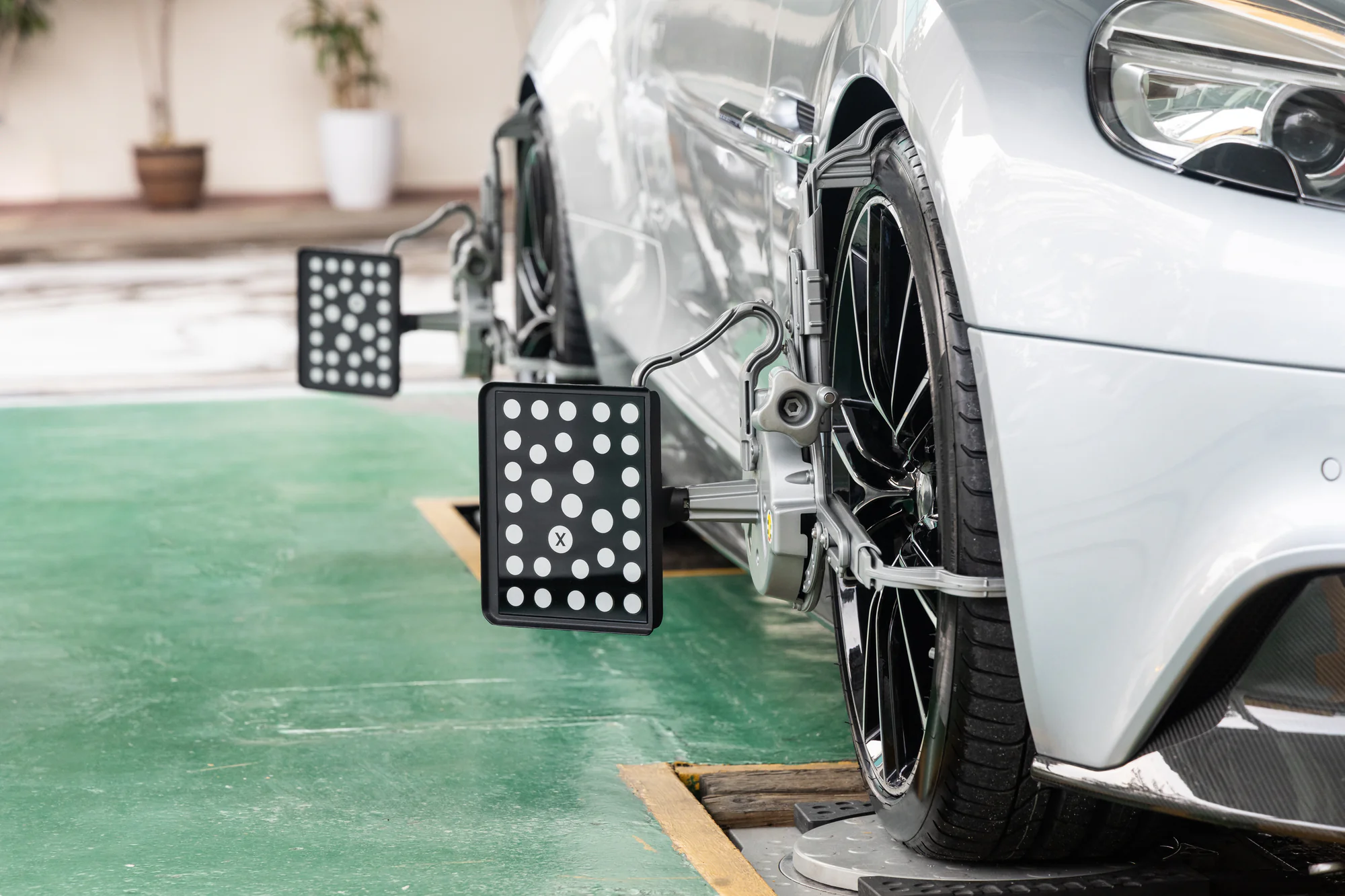 A close-up view of a silver car in NY undergoing wheel alignment by Mobile Repair & Replacement Suffolk County, with alignment sensors on the tires and black-and-white checkered calibration boards positioned on each wheel.