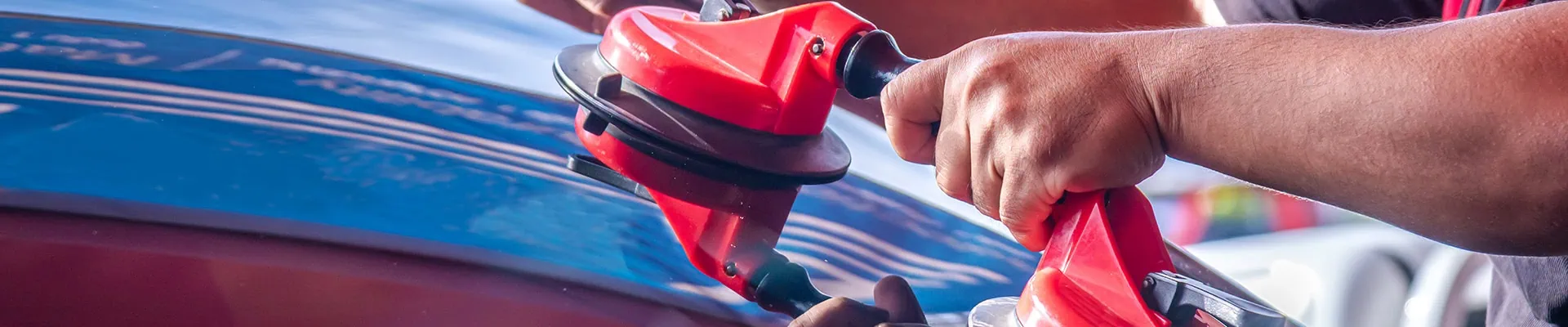 A person uses a red suction tool to lift or adjust a car windshield, showcasing expert Mobile Repair & Replacement in Suffolk County, NY, with hands gripping the handles closely.